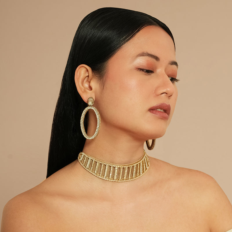 Woman wearing gold hoop earrings and a gold necklace against a beige background