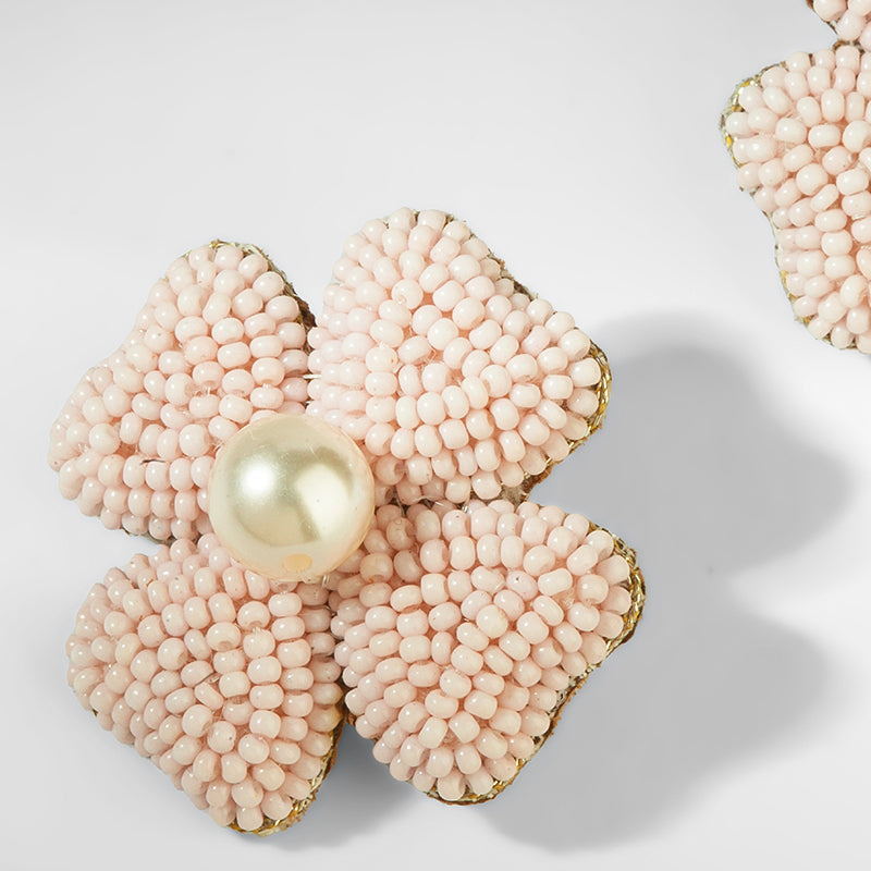 Pink beaded flower-shaped object with a central pearl on a light background