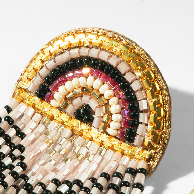 Close-up of a beaded earrings with pink, gold, and black pattern on a light gray background