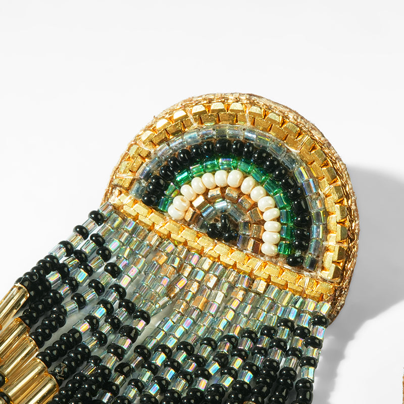 Close-up of a beaded earrings with gold, black, and green colors on a white background.