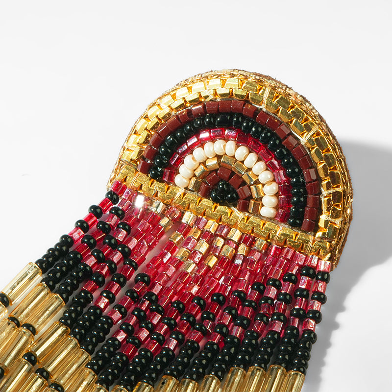 Close up of earrings with gold, red, and black beads on a white background