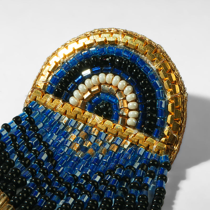 Close-up of a beaded earrings with blue, black, and gold colors on a white background.
