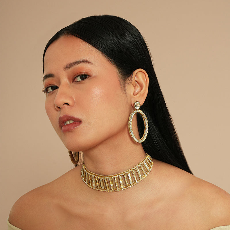 Woman wearing gold hoop earrings and a gold necklace against a beige background