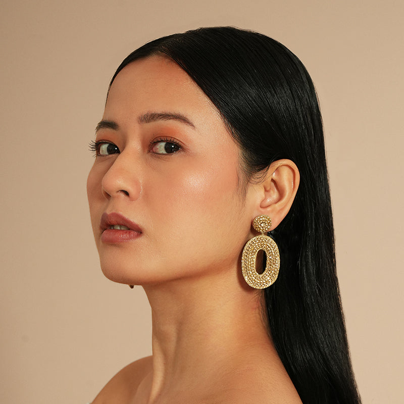Woman wearing gold earrings against a beige background