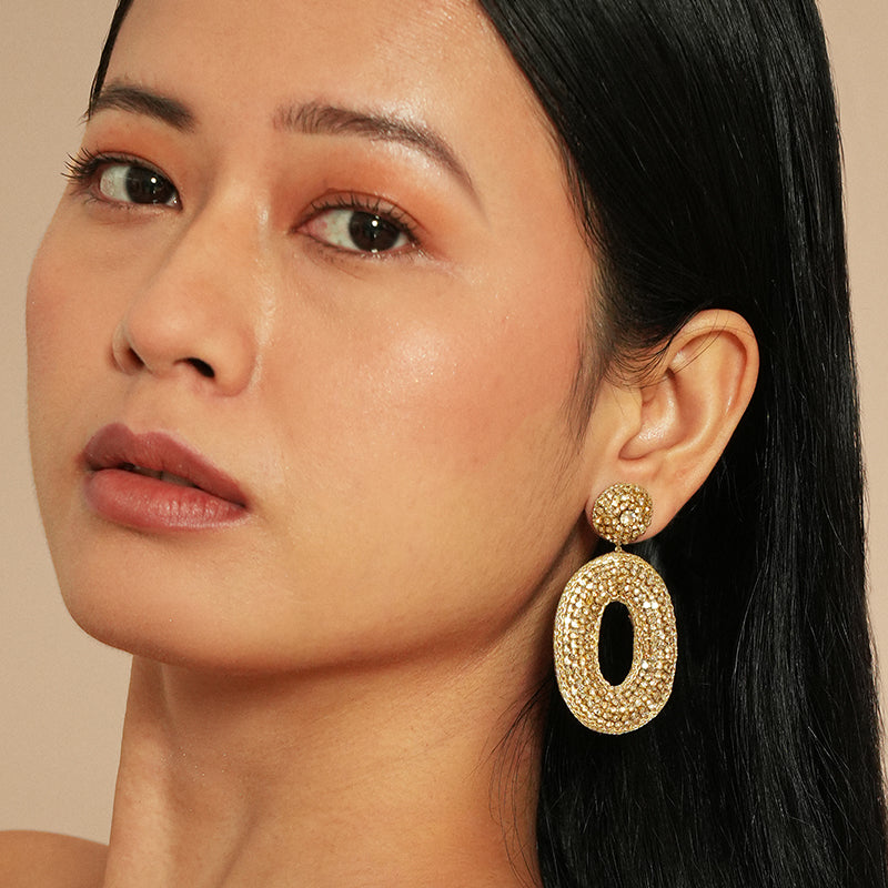 Close-up of a woman wearing gold earrings with a neutral background