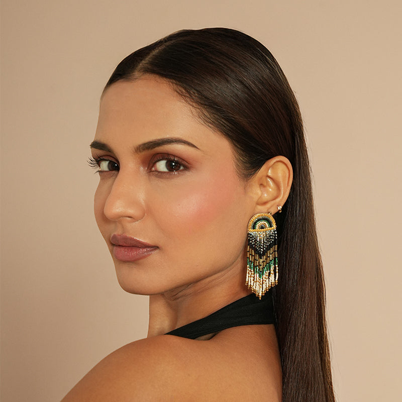 Woman wearing gold and green earrings against a beige background